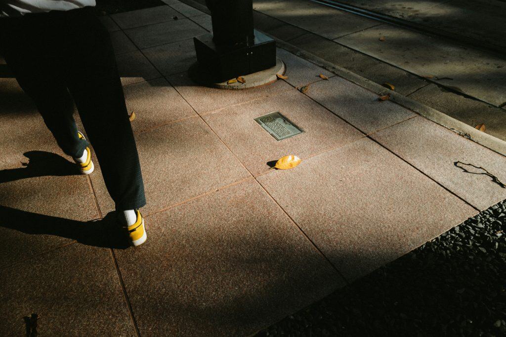 A person walking on a sidewalk, surrounded by trees and buildings, enjoying a sunny day.