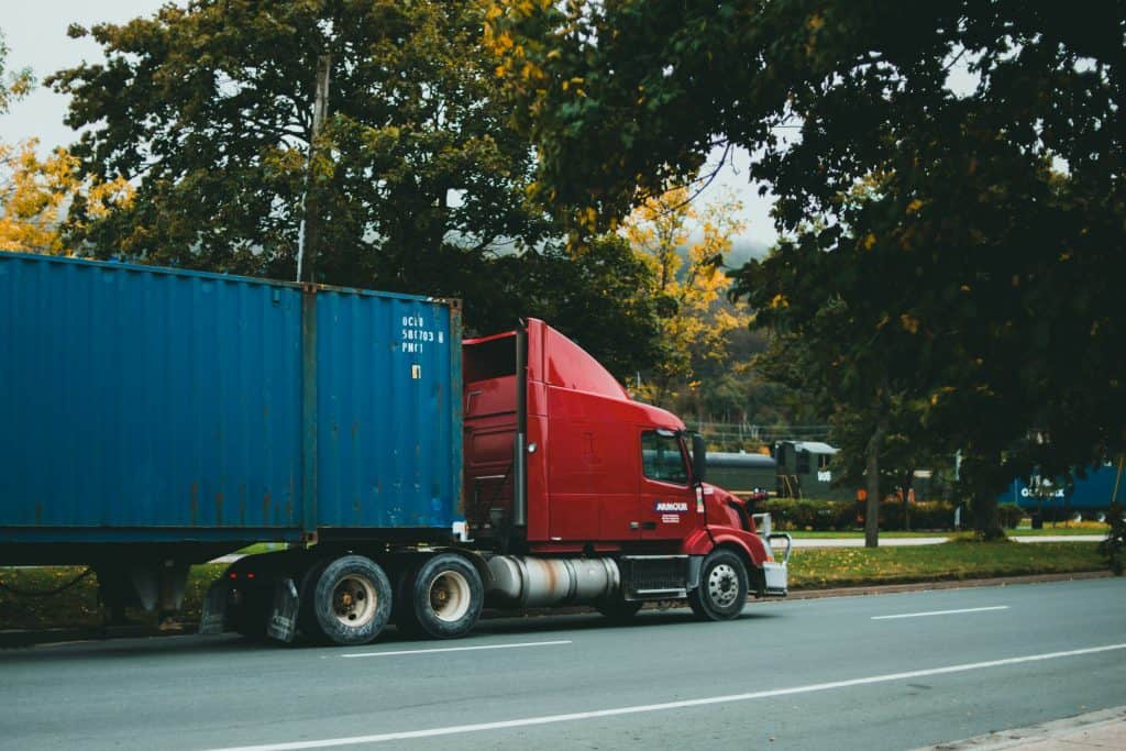 A large truck driving along a road, surrounded by trees and clear blue sky.