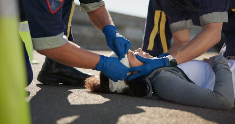 A paramedic assists a woman in standing up after an incident, providing support and care.