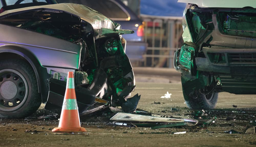 A damaged car after a head-on collision with a traffic cone, showing significant front-end impact and debris scattered around.