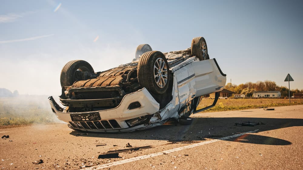 A car flipped onto its side, showing damage and debris around it.