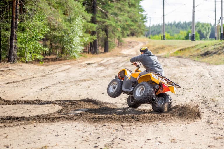 A man riding a yellow quad bike along a dirt road surrounded by greenery.