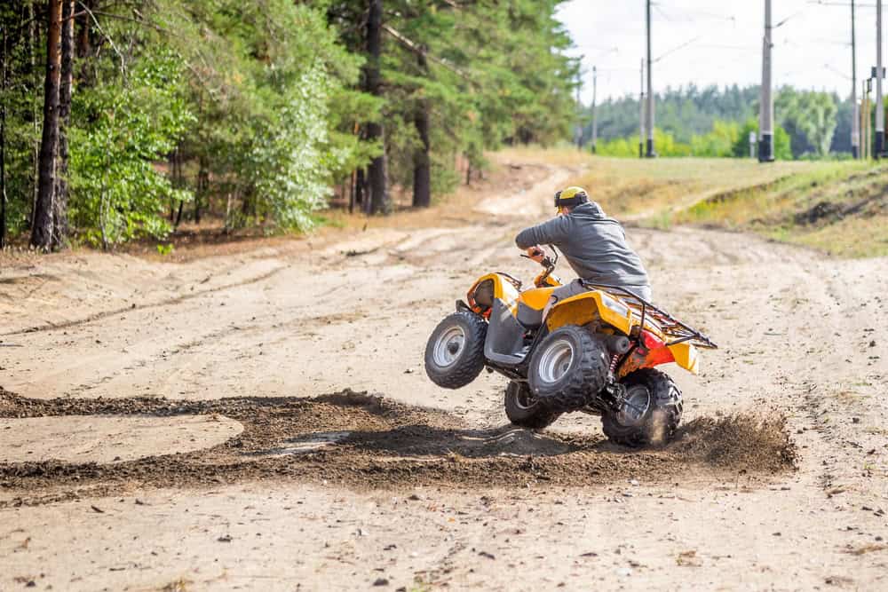 A man riding a yellow quad bike along a dirt road surrounded by greenery.
